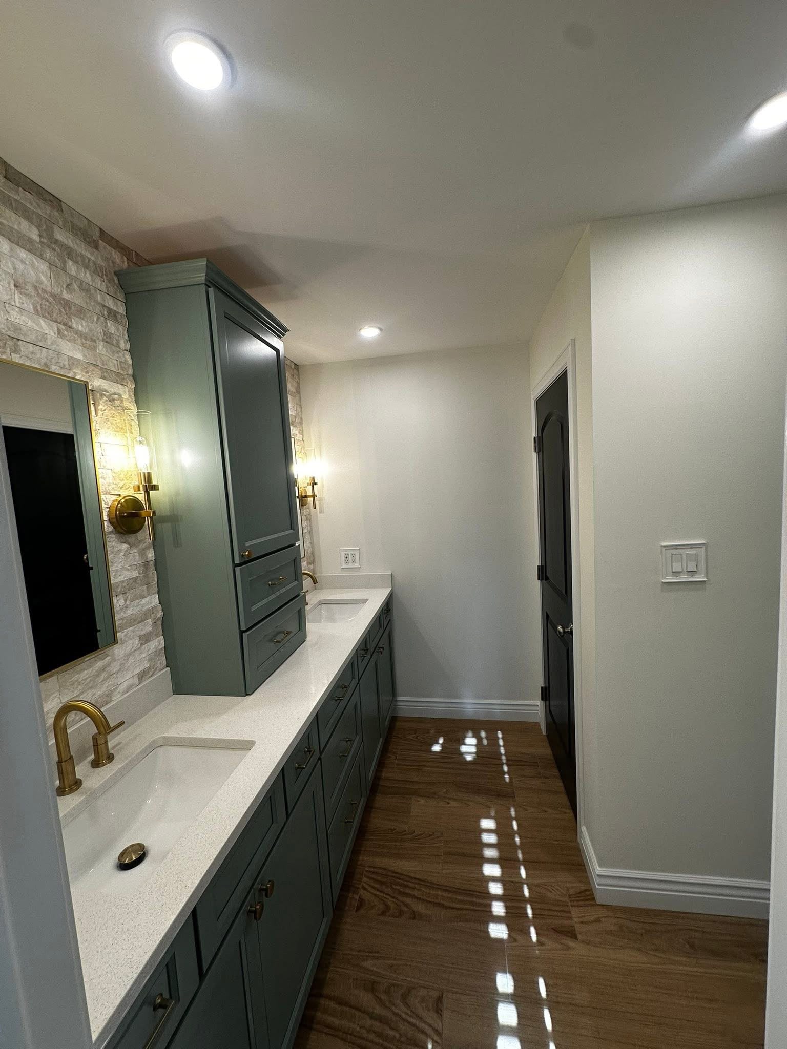 Dark bathroom vanity with stone accent wall and gold mirror